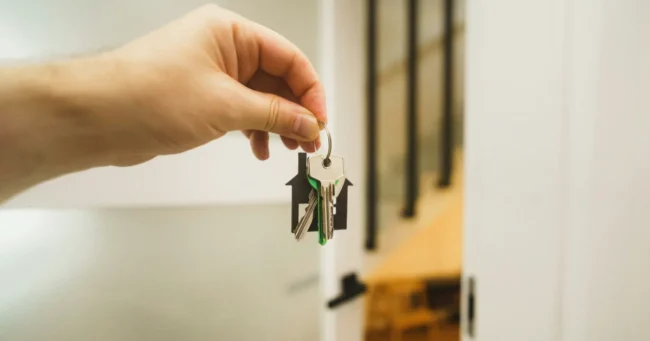 Mano que entrega las llaves de un departamento frente a una puerta abierta